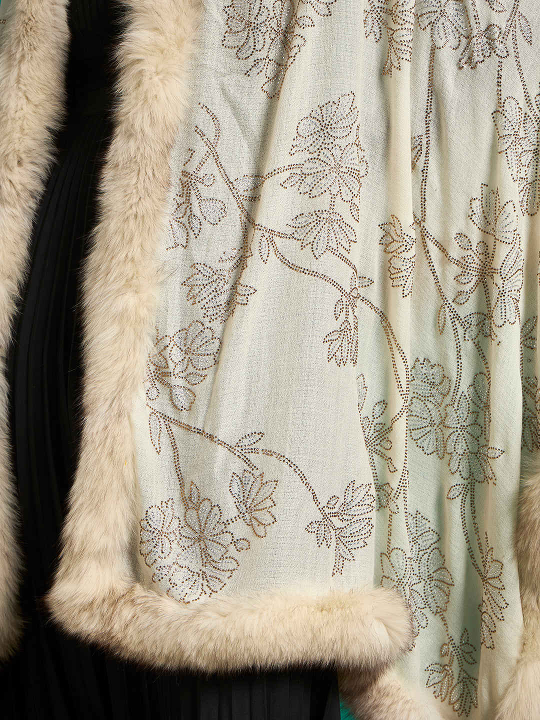 Detail of ivory shawl fabric with bronze and silver stud-outlined flowers and cream faux fur edge