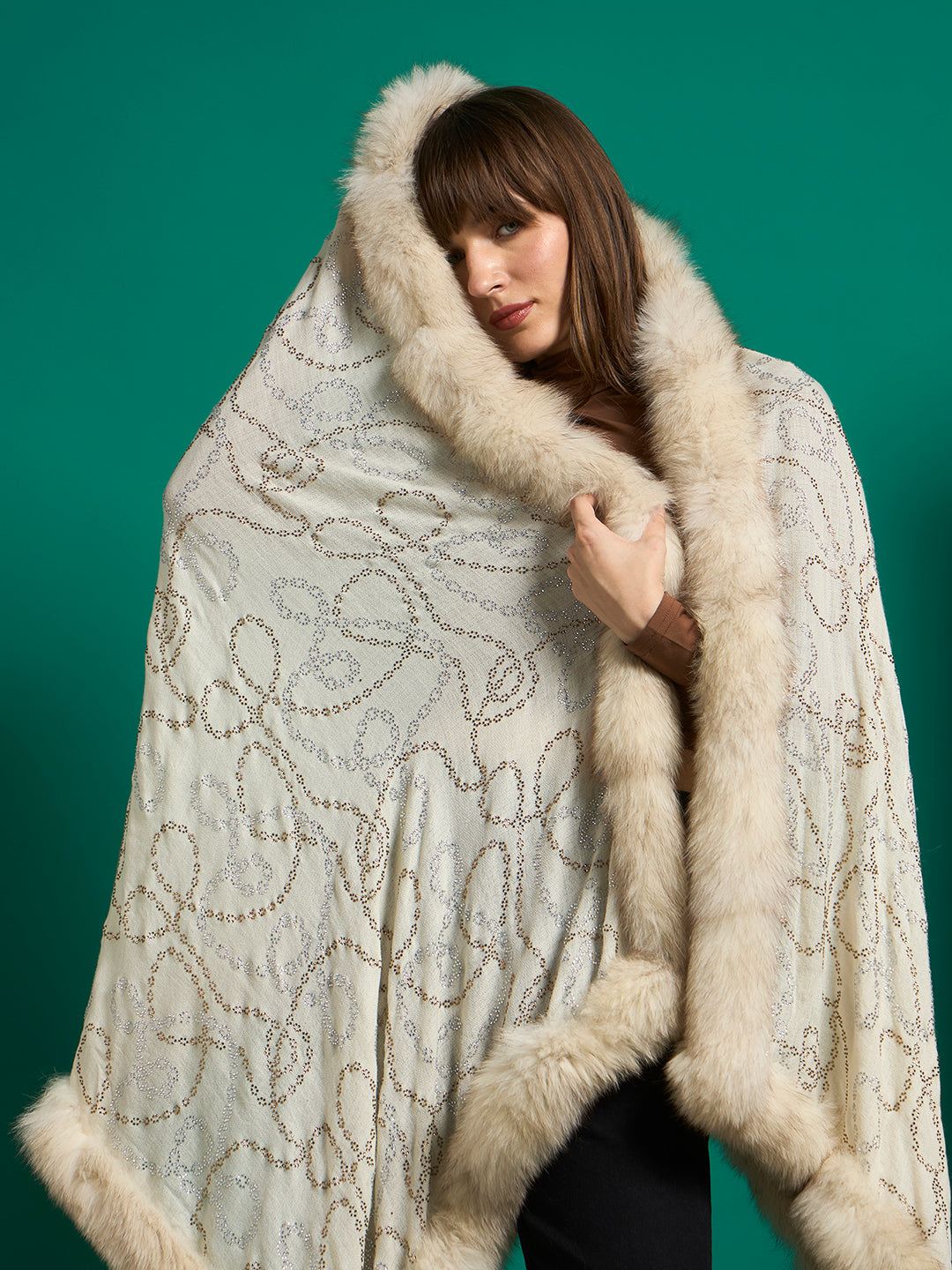 Ivory shawl with a cream faux fur border worn as a hood, showing the looping chain-link stud motif