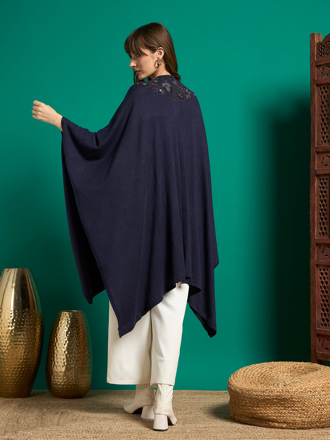 Back view of navy knit cape with small floral embellishment below the neckline and pointed side hem