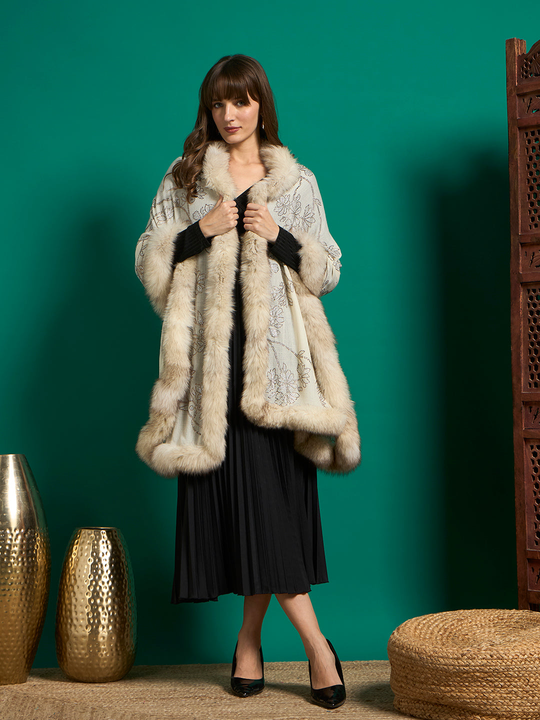 Model wearing ivory floral shawl with cream faux fur trim draped as a cape over a black pleated dress