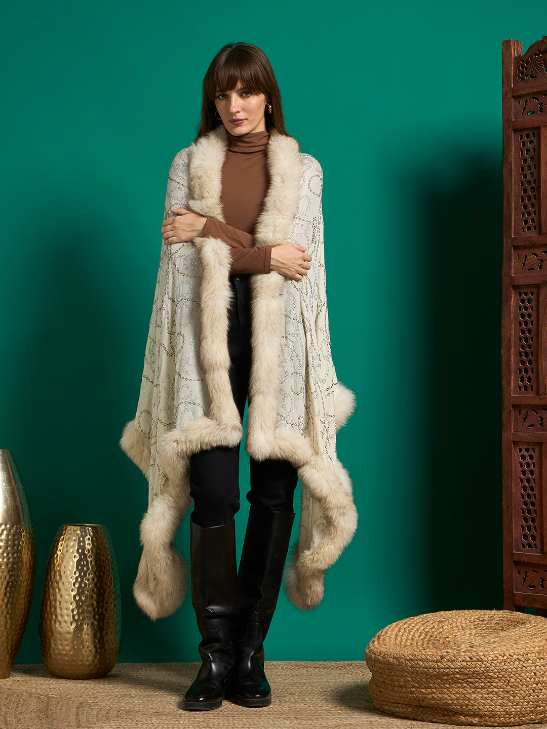 Woman wearing an ivory shawl with a chain-motif stud pattern and cream faux fur trim, draped open over a brown top