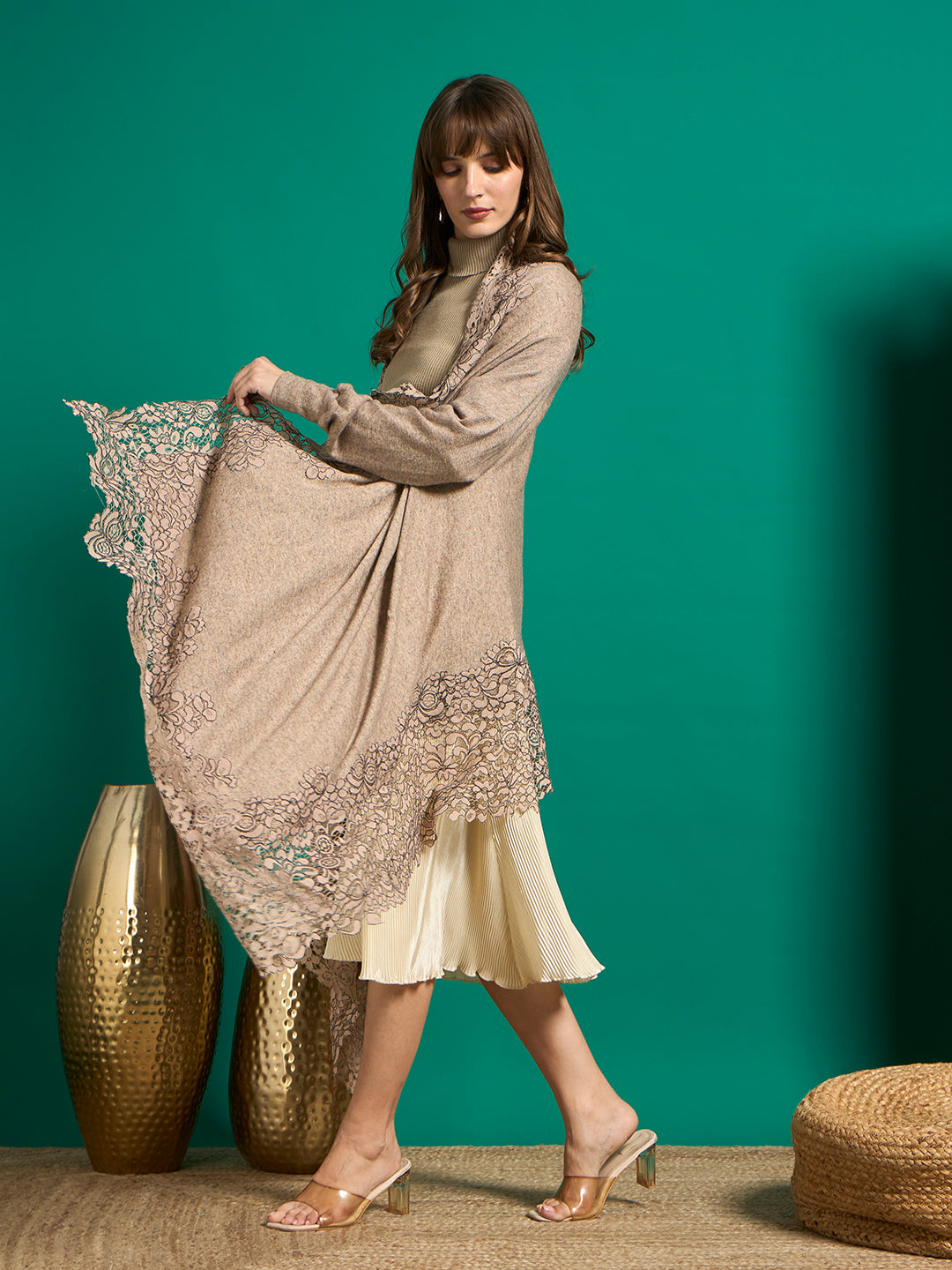 Side view of model walking in taupe cape, one side held out to show the wide floral lace hem