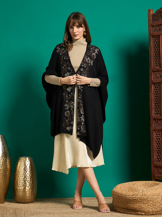 Model wearing a black open-front knit cape with silver and bronze crystal floral embellishment on the front panels